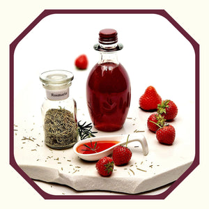 Rosmarin im Glas neben einer Flasche mit Erdbeer-Rosmarin-Essig, einem weißen Porzellanlöffel mit Essig, Erdbeeren, Rosmarin