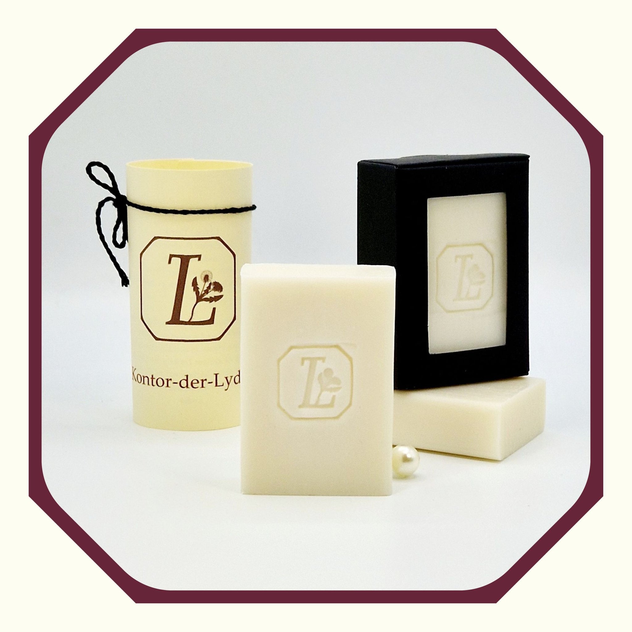 Eine Perle, eine rund gefaltete Karte mit schwarzem Schleifenband, eine Olivenseife hochkant, eine Seife schräg dahinter liegend, eine Seife Oliven-Traum hochkant auf der liegenden Seife in schwarzer Geschenkbox