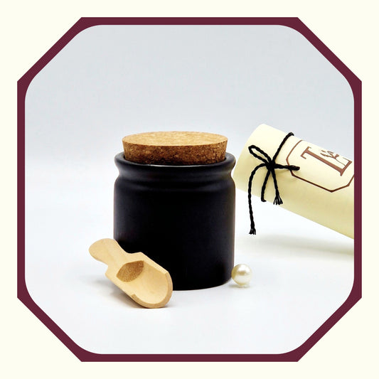 Eine Perle, eine rund gefaltete Karte mit schwarzem Schleifenband, ein Salz-Topf aus Keramik mit Korkendeckel, eine kleine Salzschaufel aus Holz