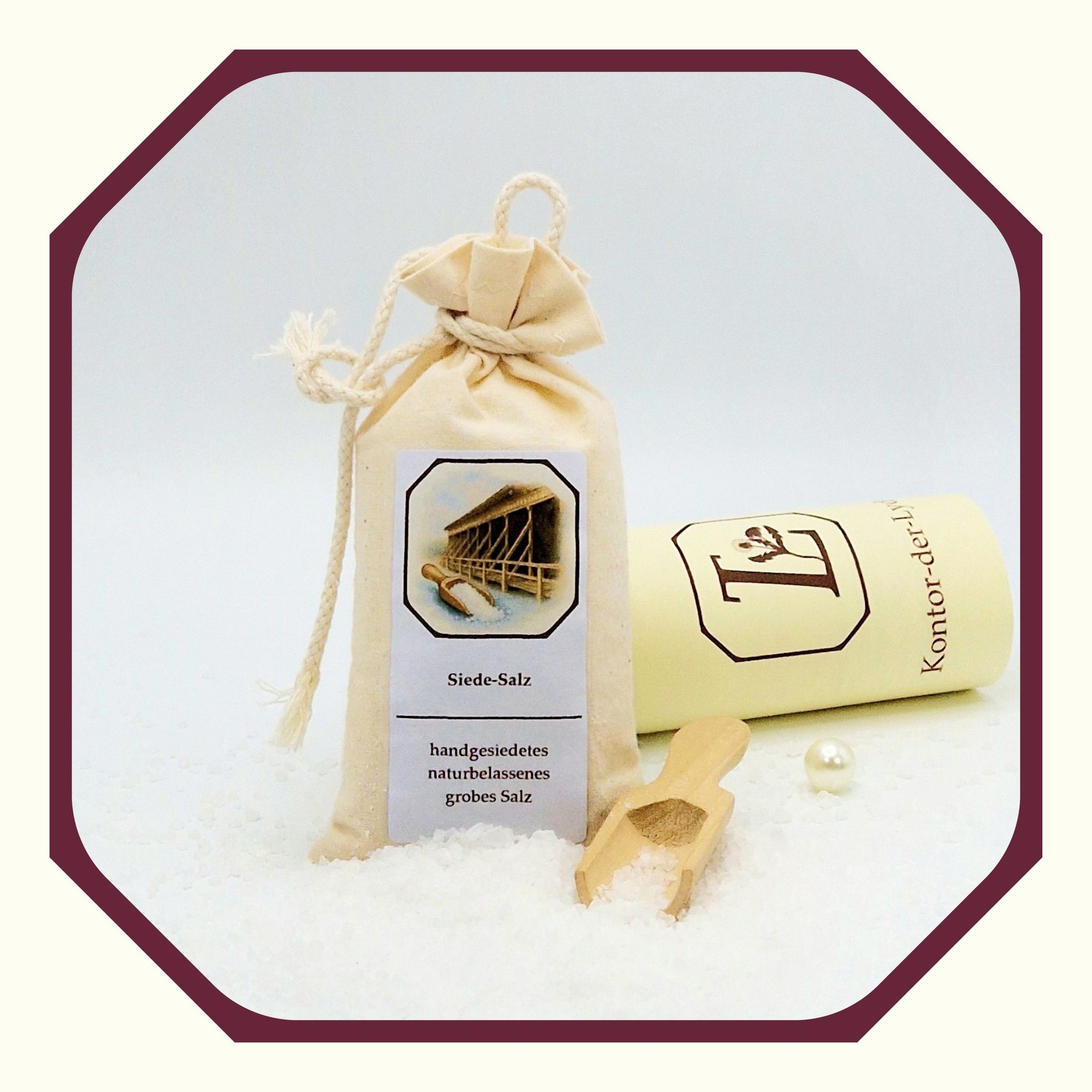 Eine Perle, eine rund gefaltete Karte mit schwarzem Schleifenband, ein Säckchen aus Leinen, gefüllt mit Siede-Salz, davor loses Siedesalz, ein kleine Salzschaufel aus Holz
