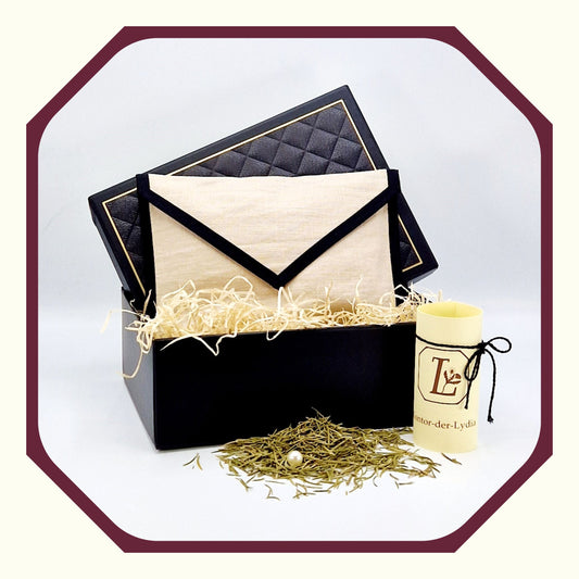 Eine Perle, eine rund gefaltete Karte mit schwarzem Schleifenband, eine selbst genähte Kräutertasche aus Leinen, in einer Luxus Geschenkbox mit Holzwolle, davor Rosmarin