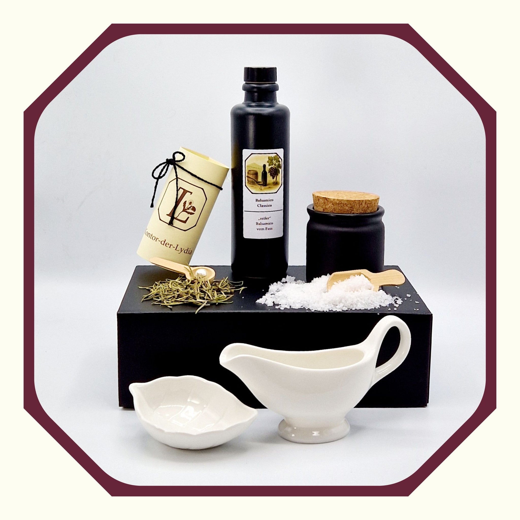 Eine Perle, eine rund gefaltete Karte mit schwarzem Schleifenband, eine schwarze Luxus Geschenkbox, darauf eine schwarze Tonflasche mit Essig Balsamico, ein schwarzer Keramik Salztopf oder Kräutertopf, Salz Fleur-de-Sel, eine kleine Salzschaufel aus Holz, Rosmarin, ein kleiner Kräuterlöffel aus Holz, davor eine weiße Sauciere und eine kleine weiße Fingerfood Schale oder Salzschale in Blattform